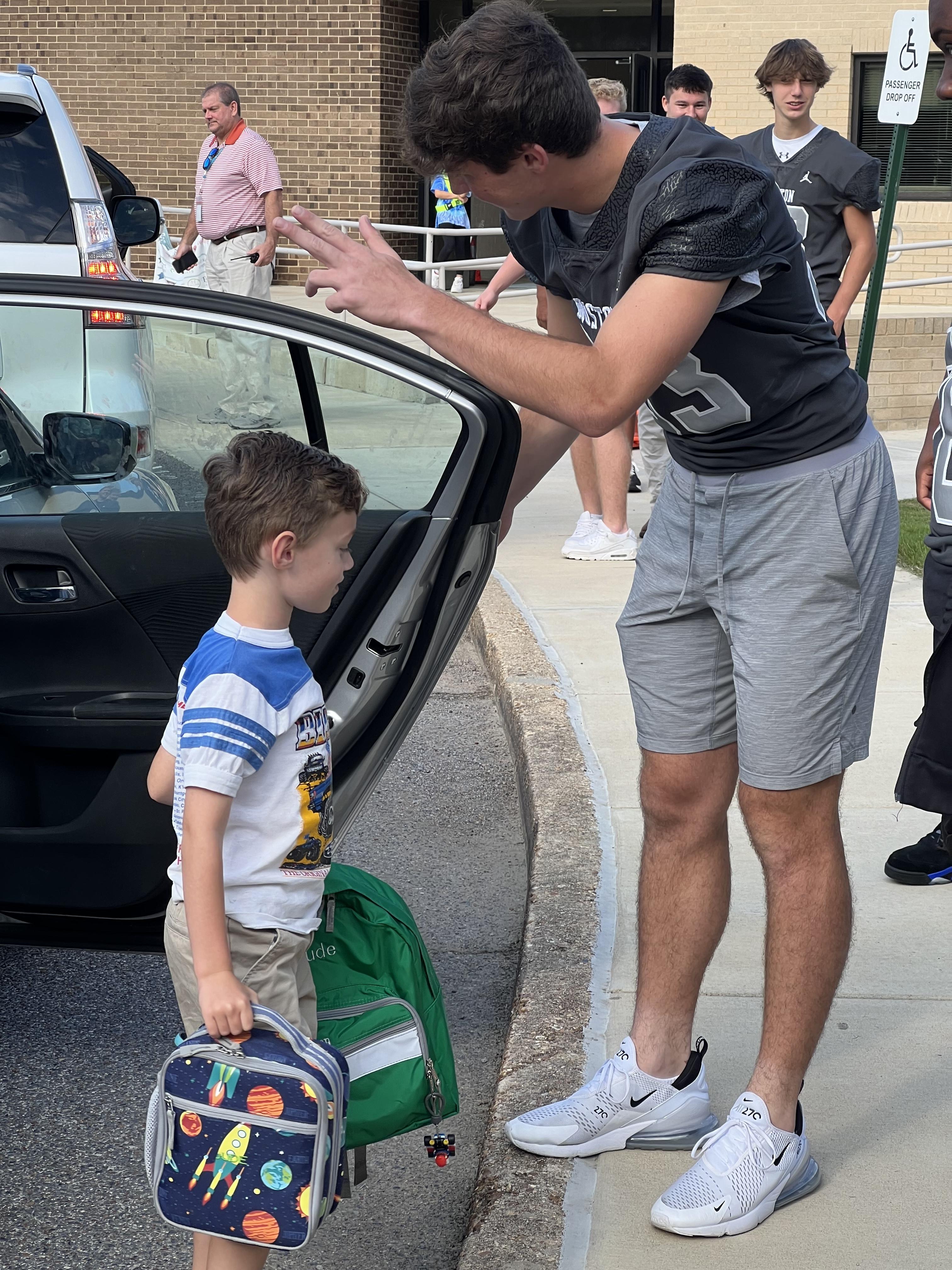 football player helping elementary student out of car